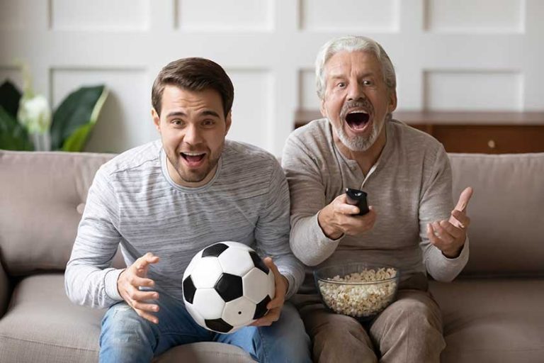 Overjoyed mature man father with adult son watching tv, match together