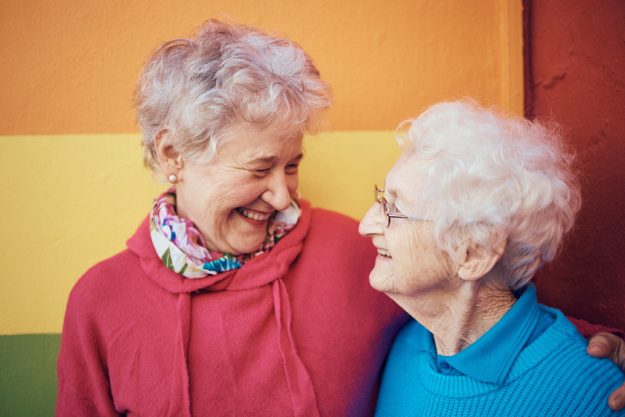 Friends, happy and retirement with a senior woman and friend outdoor together on a color wall background. Smile, freedom and glasses with mature female friendship bonding or laughing outside A Guide To Making Friends In Magnolia, NJ Senior Communities