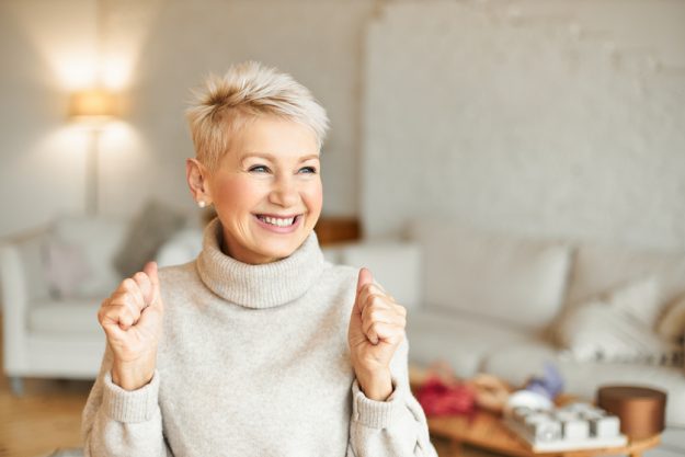 Indoor shot of fashionable overjoyed mature female in turtleneck sweater enjoying positive news, having ecstatic facial expression, laughing and clenching fists. Success and achievements concept These 7 Senior Living Activities In Barrington, NJ Will Keep You Excited
