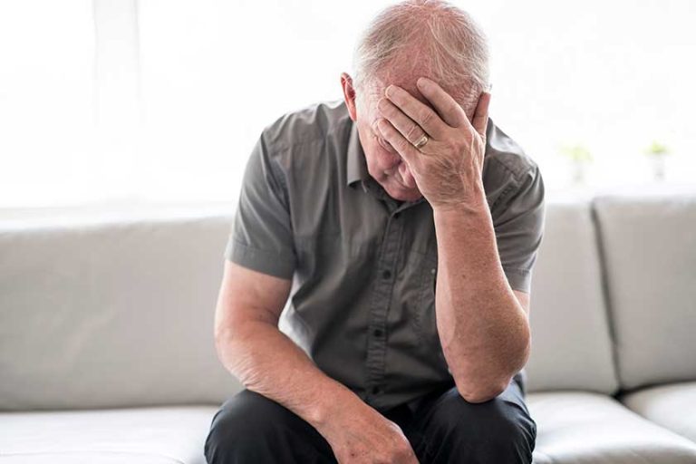 Senior man thinking and sitting on sofa at home like sad