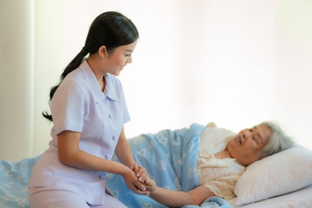 Nurse sitting on a hospital bed next to an older woman helping h What Matters The Most For Your Loved Ones When Choosing Senior Assisted Living