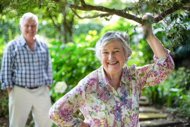 Portrait of senior woman with husband standing in background at back yard How Senior Communities in East York, PA Can Help You Find Happiness in Golden Years