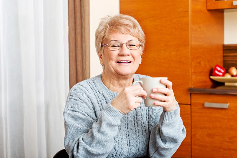 Senior woman sitting at the desk and drinking coffee