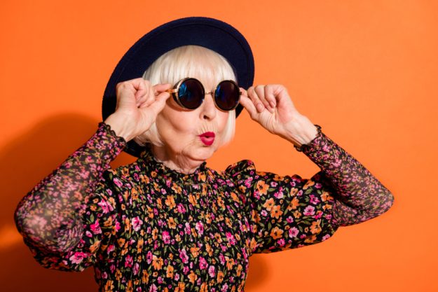 Portrait of shocked amazed surprised cool grandmother look copyspace touch sunglasses isolated on orange color background Portrait of shocked amazed surprised cool grandmother look copyspace touch sunglasses isolated on orange color background