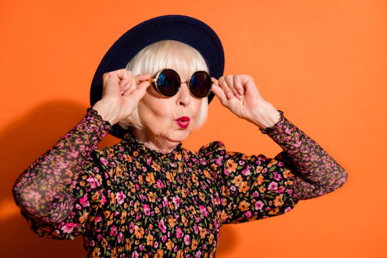 Portrait of shocked amazed surprised cool grandmother look copyspace touch sunglasses isolated on orange color background