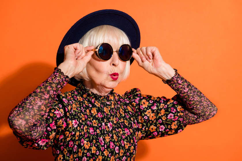 Portrait of shocked amazed surprised cool grandmother look copyspace touch sunglasses isolated on orange color background