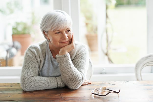 Lost in pleasant memories. A senior woman sitting at her kitchen table lost in thought. Lost in pleasant memories. A senior woman sitting at her kitchen table lost in thought.