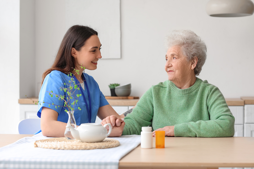 Young caregiver with senior woman holding hands in kitchen
