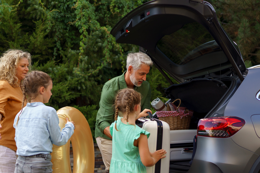 Family with little children loading car and waiting for charging car before going on holiday.