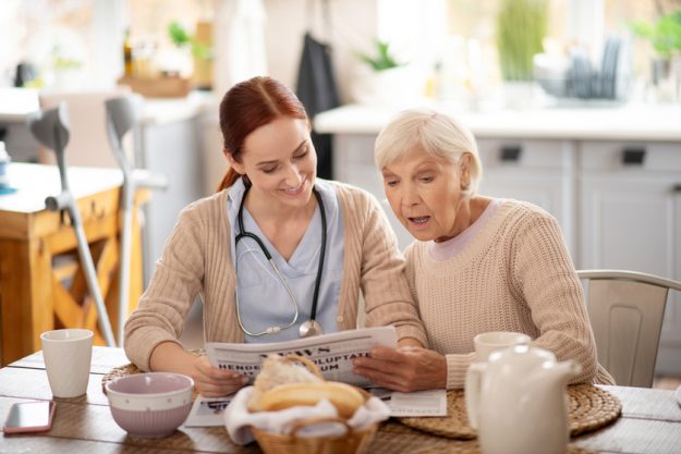 Caregiver reading morning news for retired woman Caregiver reading morning news for retired woman
