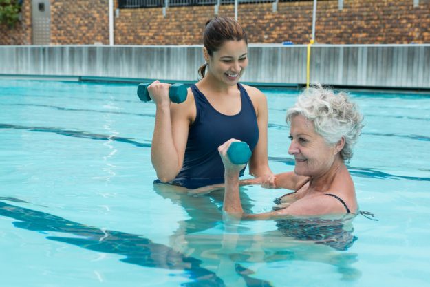 Female coach assisting senior woman in lifting dumbbells Female coach assisting senior woman in lifting dumbbells