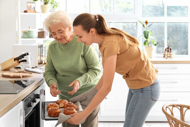 Senior woman with her granddaughter taking buns from oven in kitchen Senior woman with her granddaughter taking buns from oven in kitchen