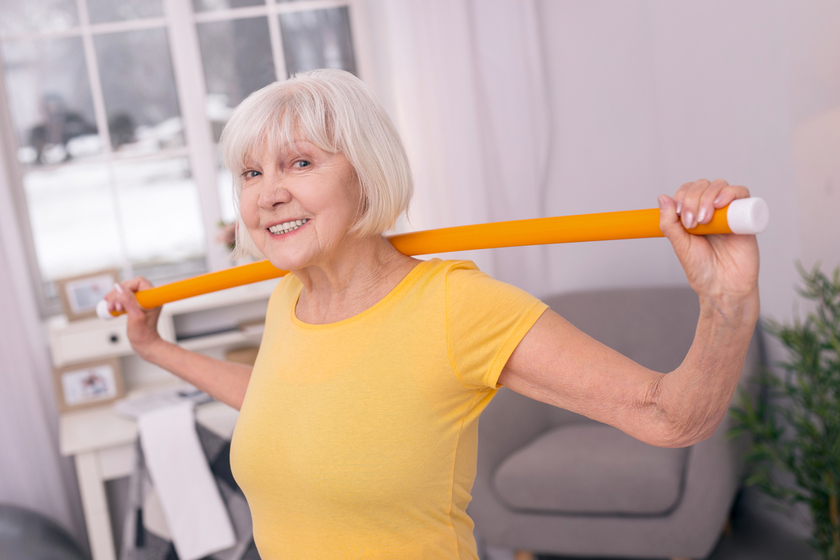 Cheerful elderly woman posing while exercising with health wand