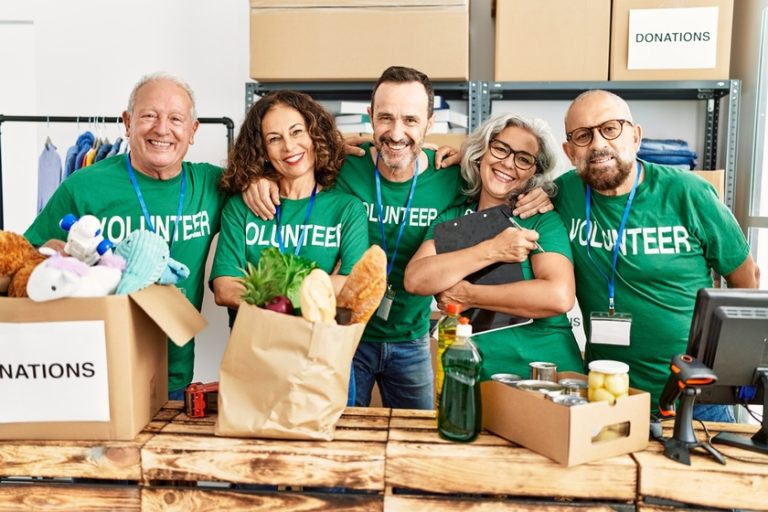 Group of middle age volunteers smiling happy and hugging standing at charity center.