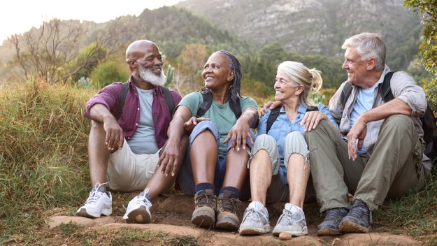 Active Senior Friends Sitting Taking A Break Hiking Through Countryside Together