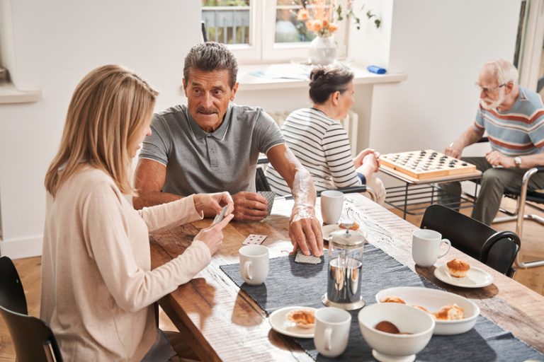 Male pensioner sitting at the table with his caregiver and drinking tea