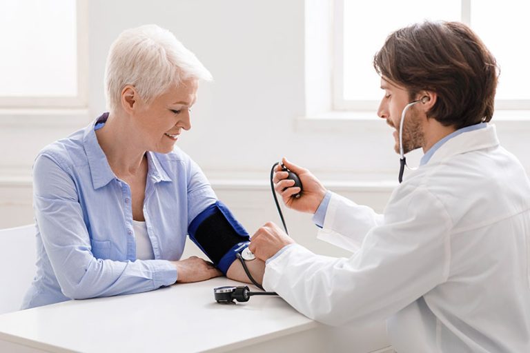 Doctor measuring blood pressure of senior woman at clinic