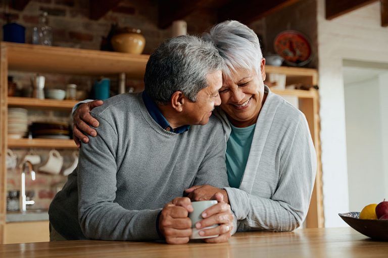 Happily retired elderly multi cultural couple smiling heads together wife holding husband in modern kitchen