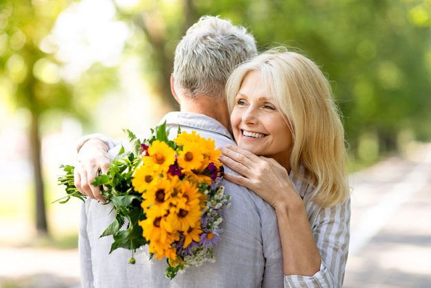 Happy beautiful senior woman holding flower bouquet embracing her husband