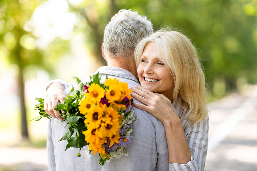 Happy beautiful senior woman holding flower bouquet embracing her husband Happy beautiful senior woman holding flower bouquet embracing her husband