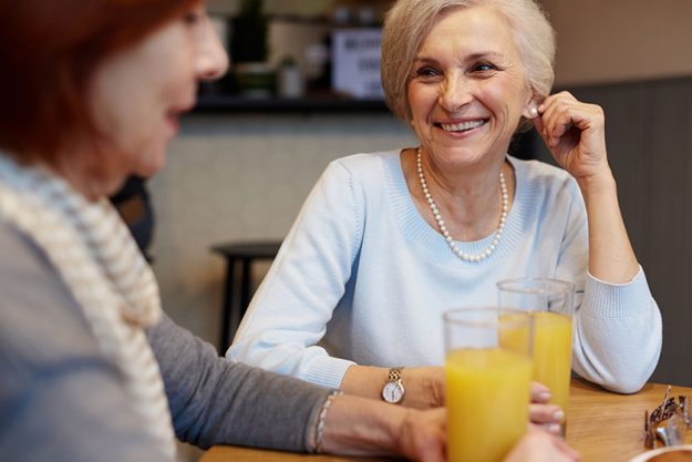 Happy retired woman juice talking her friend cafe