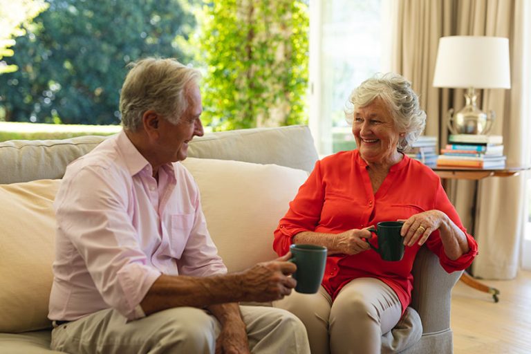 Senior caucasian couple sitting sofa together drinking coffee living room