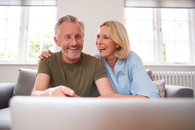 Senior couple sitting sofa lounge home using laptop together