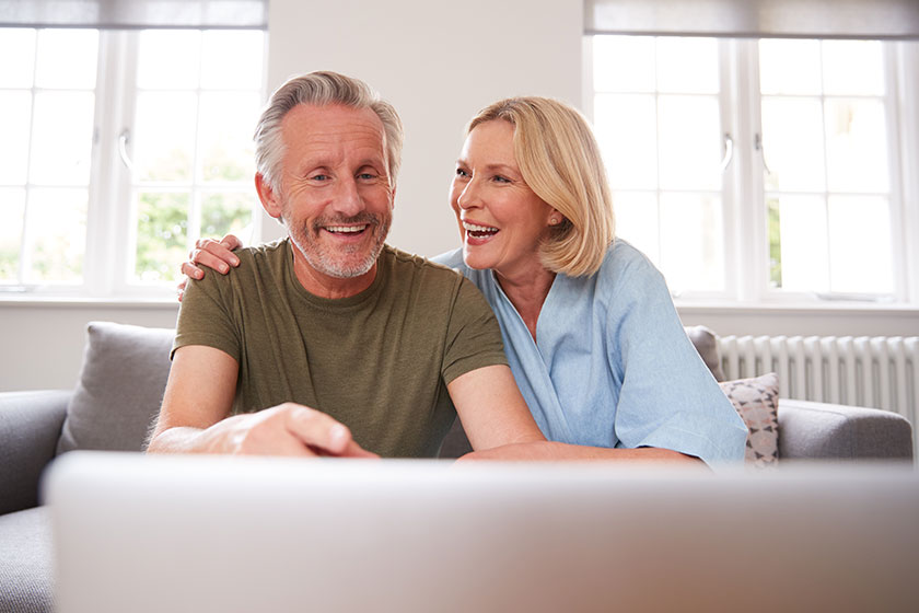 Senior couple sitting sofa lounge home using laptop together