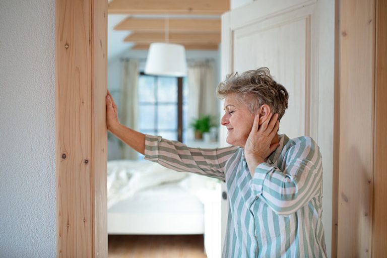 Senior woman standing by door at home getting up in the morning