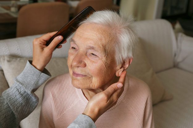 Unrecognizable woman brushing elderly lady hair comb granddaughter helping granny