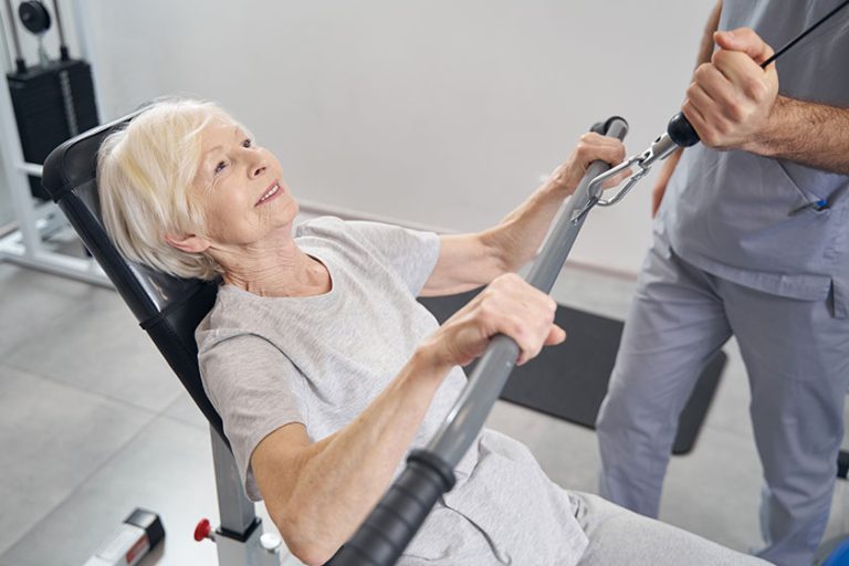 Aged woman on seat of gym equipment doing arm exercise