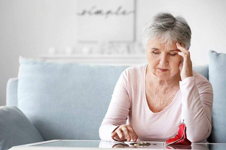 Sad senior woman counting money home