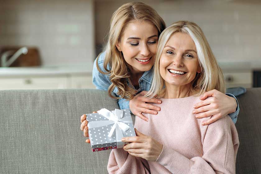 Loving young adult daughter makes an unexpected surprise to her mature attractive mom, gives her a gift. Friendship of mom and daughter