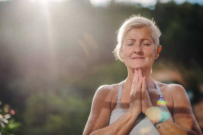 A senior woman standing outdoors on a terrace in summer, doing yoga. A senior woman standing outdoors on a terrace in summer, doing yoga.
