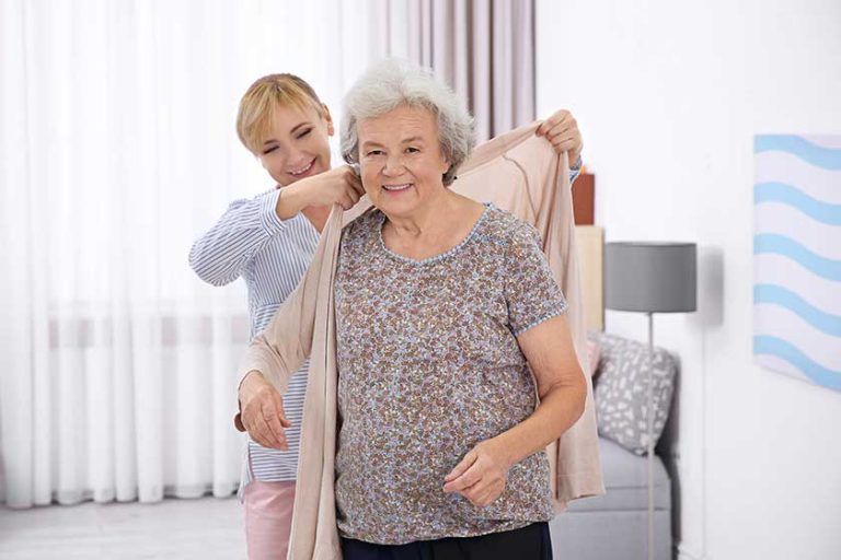 Caregiver helping senior woman to put on cardigan at home