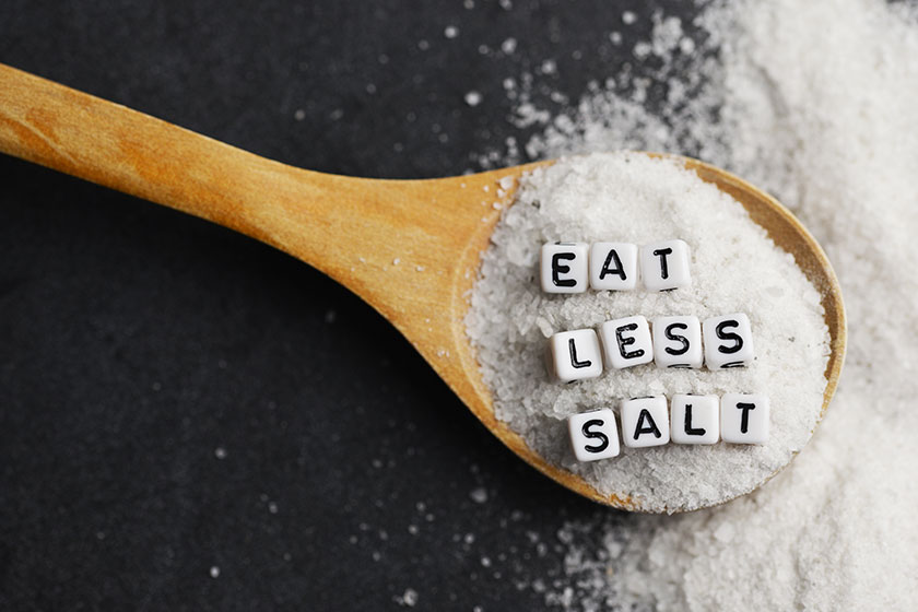 Eat less salt in order to reduce blood pressure or hypertension risk with sprinkled salt on dark background Eat less salt in order to reduce blood pressure or hypertension risk with sprinkled salt on dark background