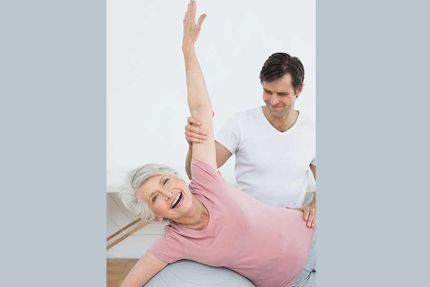 Physical therapist assisting senior woman with yoga ball