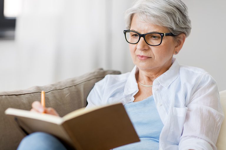 Senior woman writing to notebook or diary at home