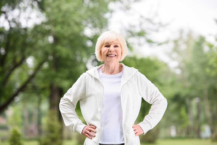 Smiling elderly sportswoman standing on green lawn in park Smiling elderly sportswoman standing on green lawn in park