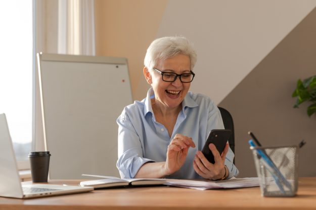 Confident stylish european middle aged senior woman using smartphone at workplace. Stylish older mature 60s gray haired lady businesswoman with cell phone in office. Boss leader using internet apps — Photo
