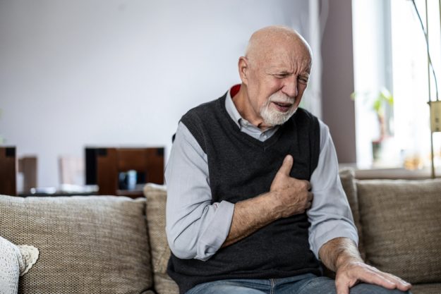 Senior man suffering from chest pain while sitting on sofa at home — Photo Senior man suffering from chest pain while sitting on sofa at home — Photo