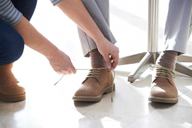 Adult Daughter Helping Senior Tie Shoelaces