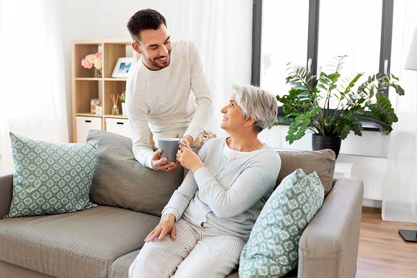 Adult son bringing coffee to senior mother at home
