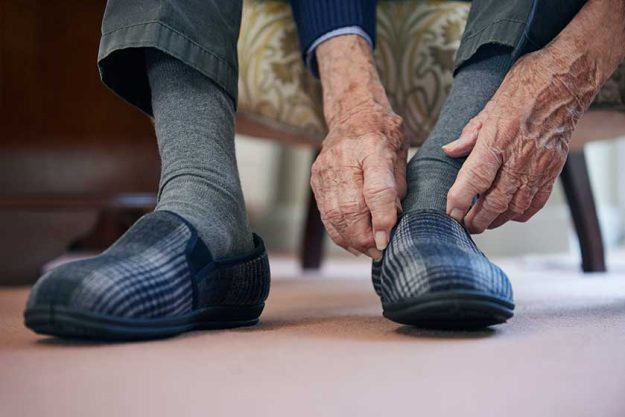 Close Up Of Senior Man Putting On Slippers To Keep Feet Warm In Cost Of Living Crisis Close Up Of Senior Man Putting On Slippers To Keep Feet Warm In Cost Of Living Crisis