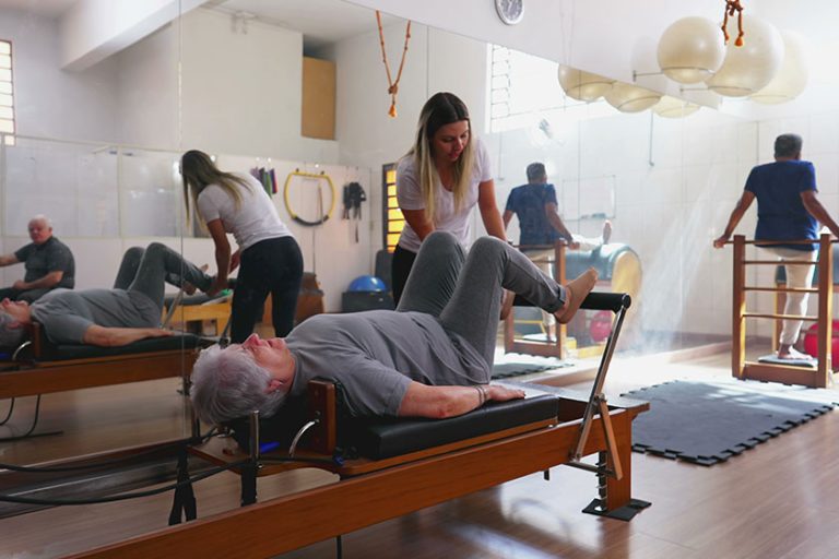 Female Pilates Instructor coaching Elderly Woman to use Machine. Old Age Exercise workout routine lifestyle