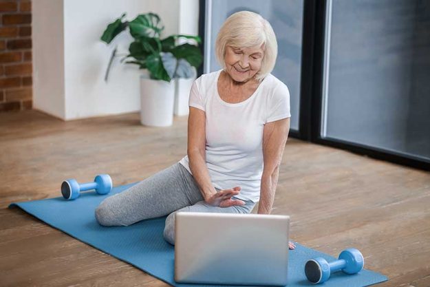Gray-haired senior woman sitting on the floor and having a video call