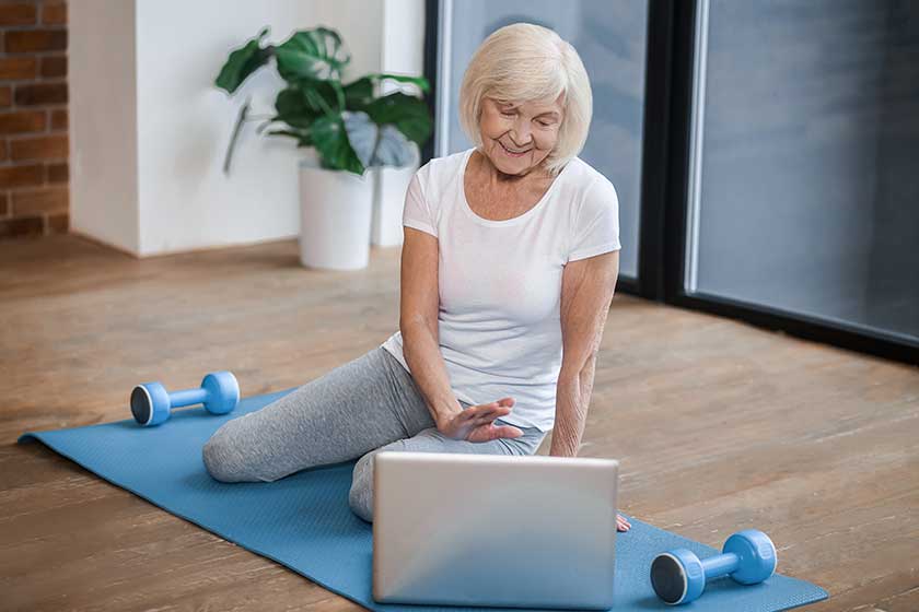 Gray-haired senior woman sitting on the floor and having a video call