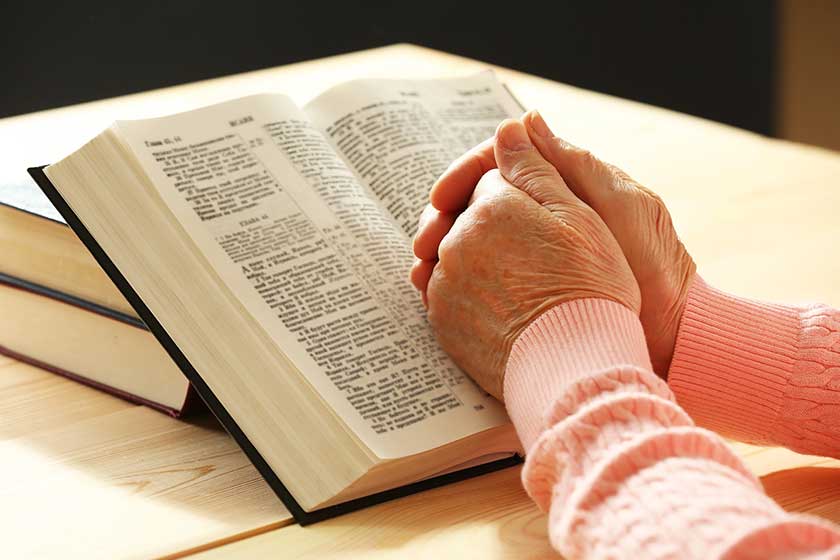 Hands of old woman with Bible on table and dark background