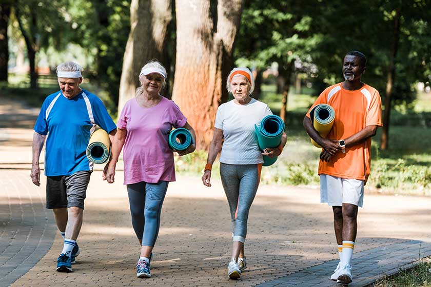 Happy senior and multicultural pensioners holding fitness mats and walking in walkway in park Happy senior and multicultural pensioners holding fitness mats and walking in walkway in park