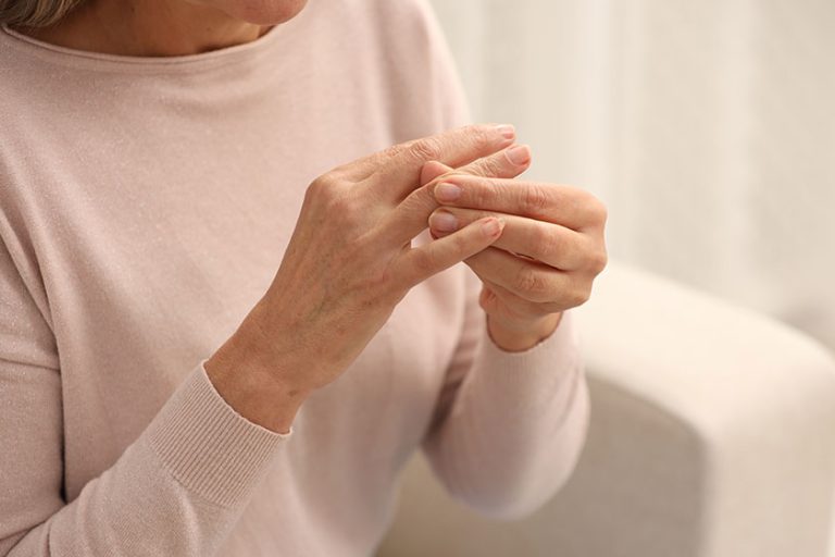 Mature woman suffering from pain in hand indoors, closeup. Rheumatism symptom